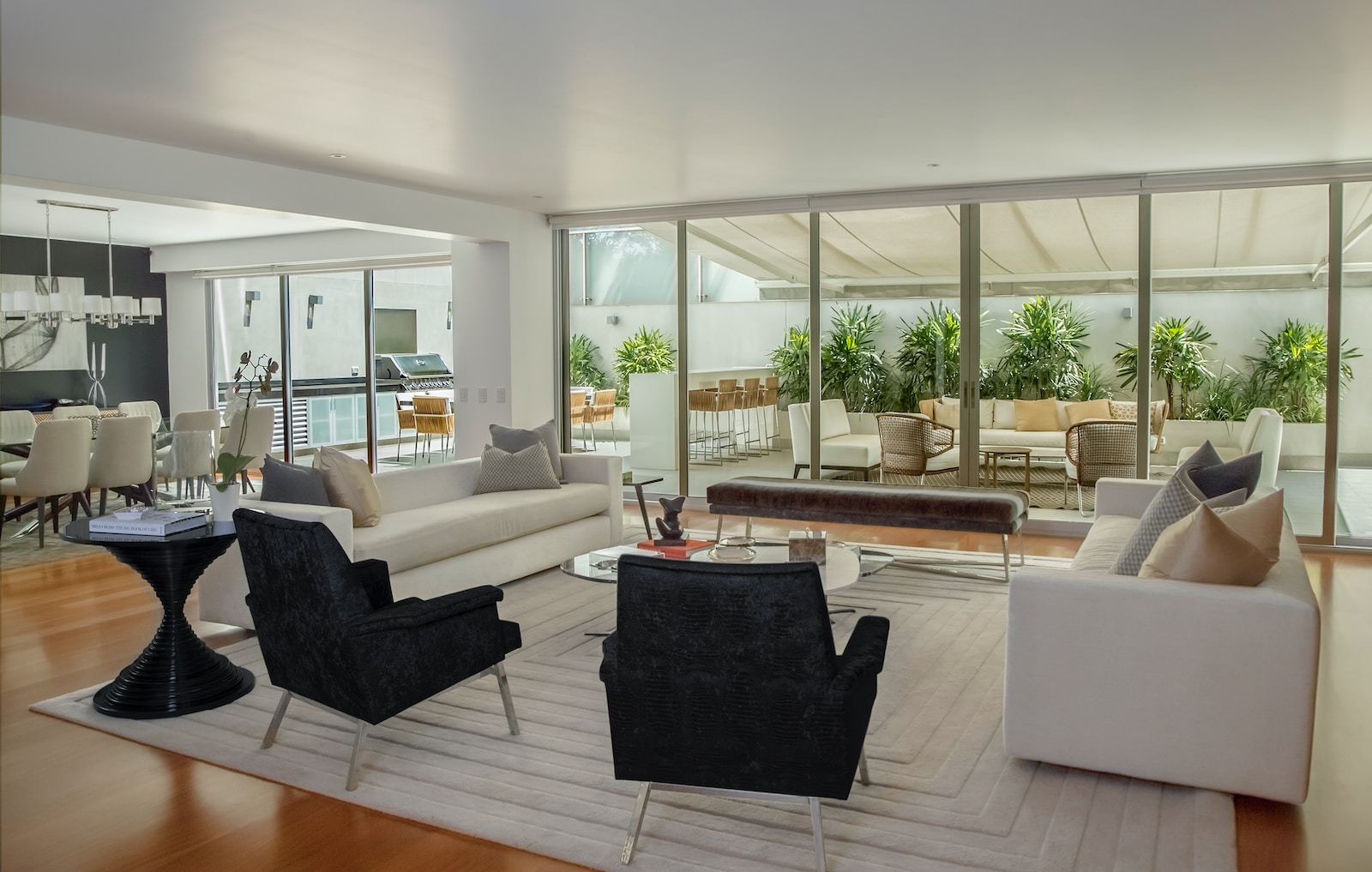 Modern living room with elegant furniture, large windows, and a view of a lush patio garden