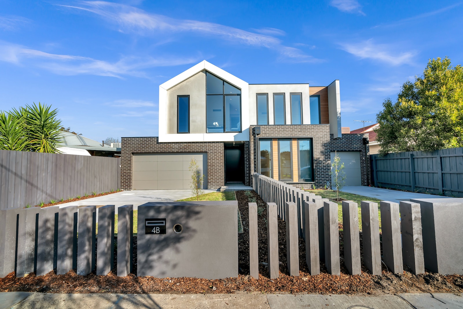 Modern two-story house with unique black and white facade, manicured garden, and geometric fence under blue sky