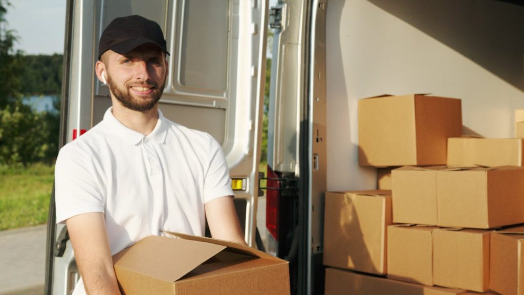 Smiling delivery person holding a box near a van with packages in the background